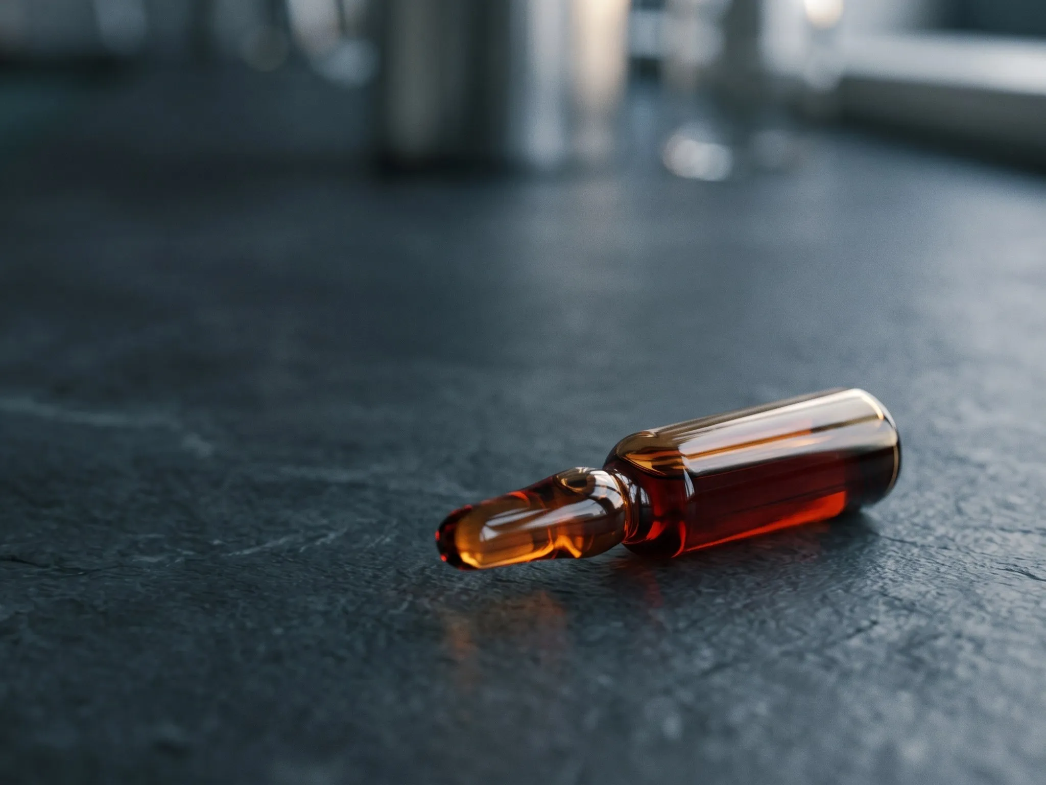 Glass ampoule of red-brown liquid on a slate surface
